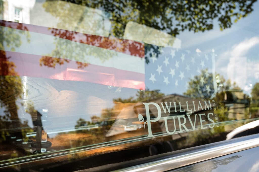 Photo of a coffin draped in an American flag, sitting in the back of a William Purves hearse, awaiting repatriation home with a family member on the same flight as their coffin