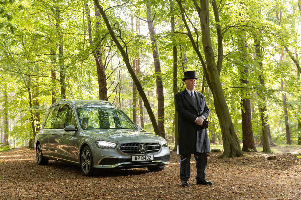 Photo of a funeral director walking in front of a Mercedes hearse while attending a funeral after a death in Scotland has occurred